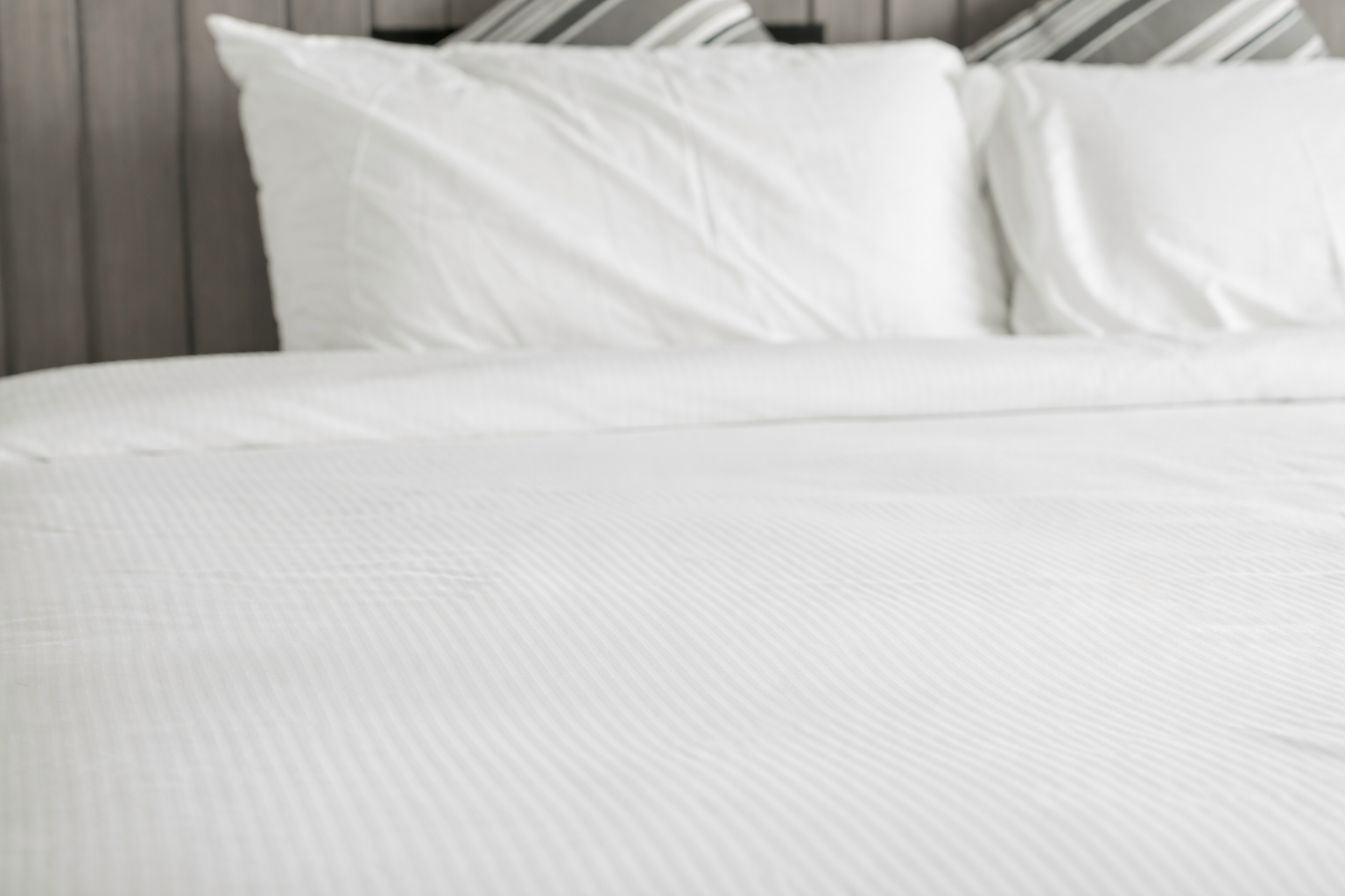 A neatly made bed with white linens, two white pillows, and two decorative pillows with gray and white stripes against a dark wooden headboard—ideal inspiration for blanket cleaning Cleveland services.