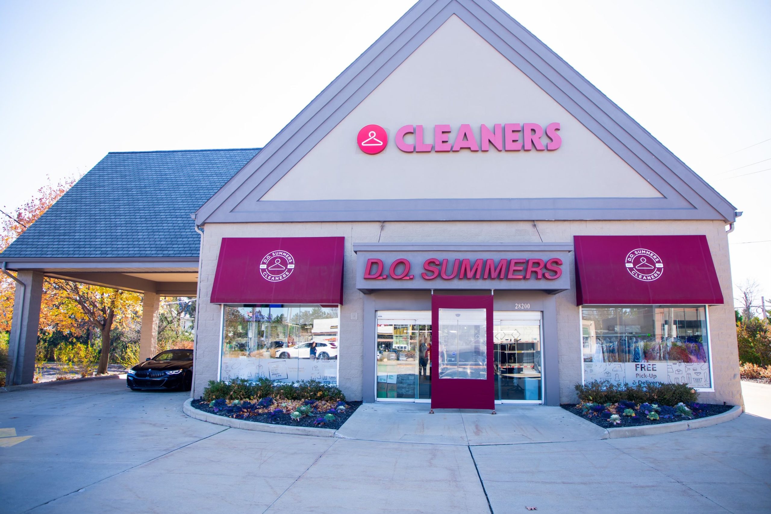 A dry cleaning shop with red signs reading "CLEANERS" and "D.O. SUMMERS" above the entrance, with a car parked on the left side.