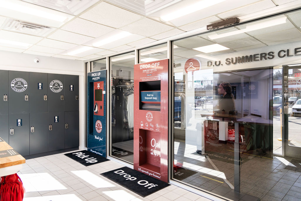 Modern dry cleaning store interior with lockers on the left and glass partition separating the pick up and drop off area from the main entrance.